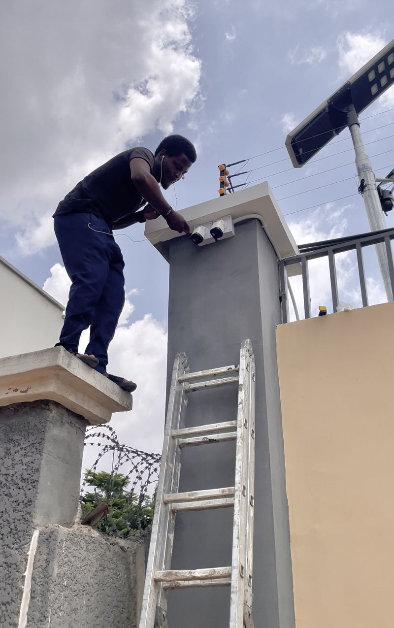 Technician installing two CCTV cameras on a gate pillar beside an electric fence